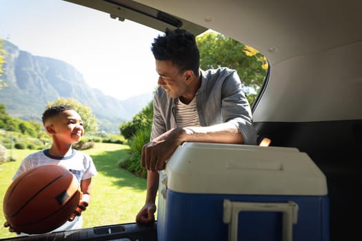 Happy african american father with son outdoors, preparing for picnic on sunny day. family enjoying quality free time together.