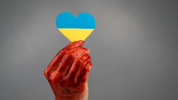 Woman with hands covered in blood holding a heart with the flag of ukraine on a white background