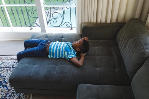 Thoughtful african american boy lying on couch looking out of window in living room. spending time alone at home.