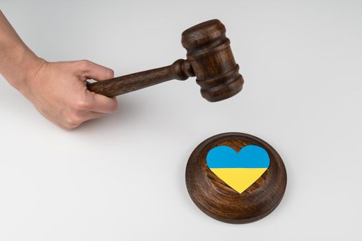 Woman hitting the judge's gavel on the heart with the flag of Ukraine on a white background