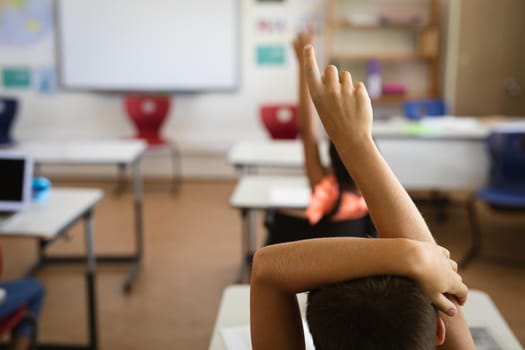 Rear view of boy raising his hand for participation in the class at elementary school. school and education concept