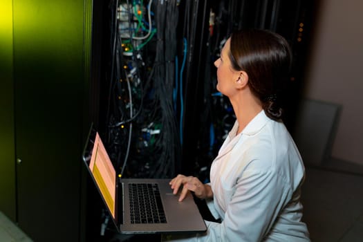 Caucasian female engineer wearing an apron using laptop while inspecting in computer server room. database server management and maintenance concept