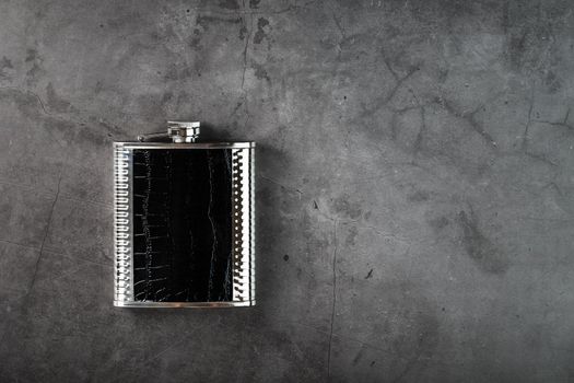 Pocket flask made of steel in leather finish with an alcoholic drink on a dark background with copy space