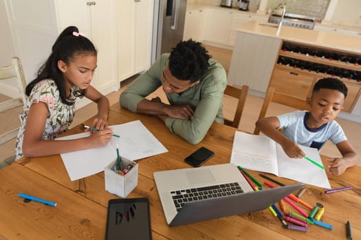 Happy african american father with daughter and son doing homework at home smiling. family domestic life, spending time learning together at home.