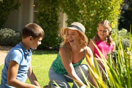Happy caucasian mother with son and daughter outdoors, gardening on sunny day. family enjoying quality free time together.