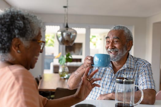 Happy african american senior couple sitting in kitchen with coffee and talking. healthy retirement lifestyle at home.