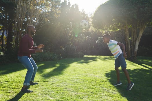 African american father with son having fun and playing football in garden. family spending time at home.