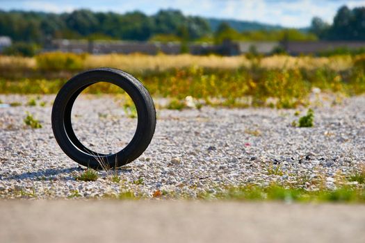 a used car wheel stands on an edge. you can see the side of the road through it