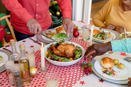 Hands of cauasian senior man cutting chicken at christmas table. christmas festivities and traditions, celebrating at home.