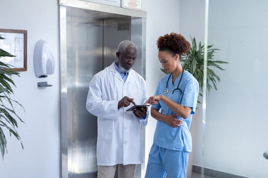 Diverse male and female doctors using tablet and discussing in hospital corridor. medical professional at work.