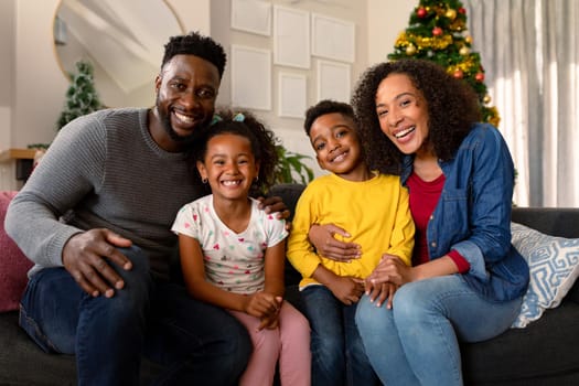 Happy african american family sitting on sofa and looking at camera. family christmas time and festivity together at home.