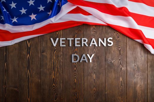 the words veterans day laid with silver metal letters on wooden board surface with crumpled usa flag on upper side, high angle flat lay perspective