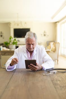 Senior caucasian male doctor sitting at table using tablet computer. medicine and healthcare services concept.
