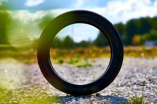 a used car wheel stands on an edge. you can see the side of the road through it