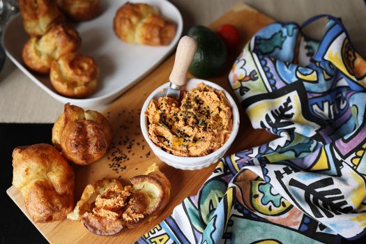 Homemade popover, which is a puffed, airy, and eggy hollow roll, is fresh from the oven and ricotta dip with sun-dried tomatoes and baked paprika in a ceramic white bowl
