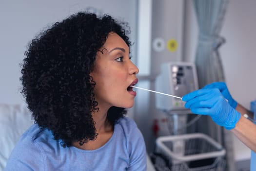 African american female patient with mouth open tested with swab test. medical professional at work during coronavirus covid 19 pandemic.