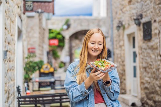 Young woman tourist eating traditional pizza in the old town of Budva. Travel to Montenegro concept.