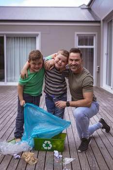 Portrait of caucasian father and two sons collecting plastic materials in a bag outdoors. plastic recycling and pollution control concept