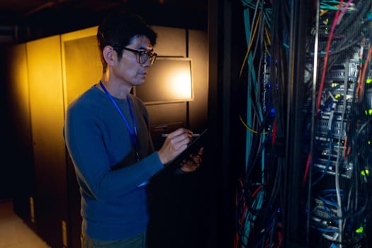 Asian male engineer writing on clipboard while inspecting in computer server room. database server management and maintenance concept