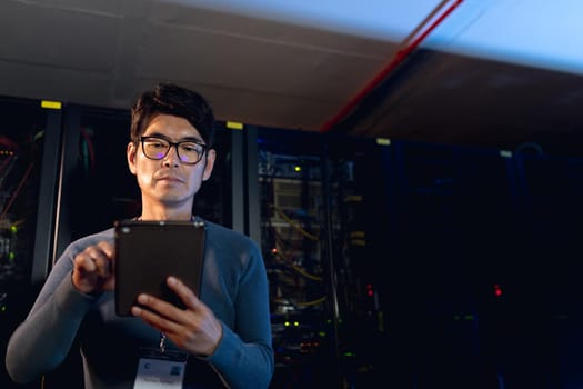 Asian male engineer using digital tablet in computer server room. database server management and maintenance concept