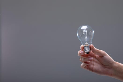 Close up of caucasian businesswoman holding light bulb, isolated on grey background. business, technology, communication and growth concept.