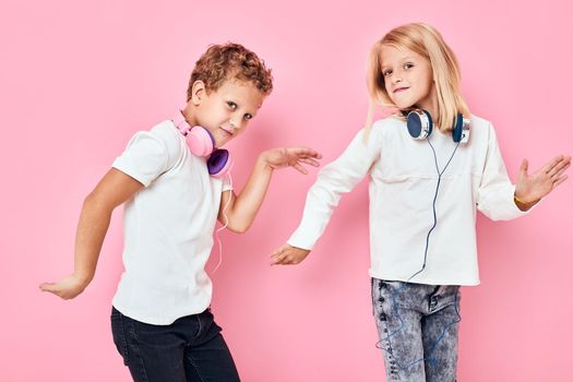 Stylish little boy and cute girl listening to music pink color background. High quality photo