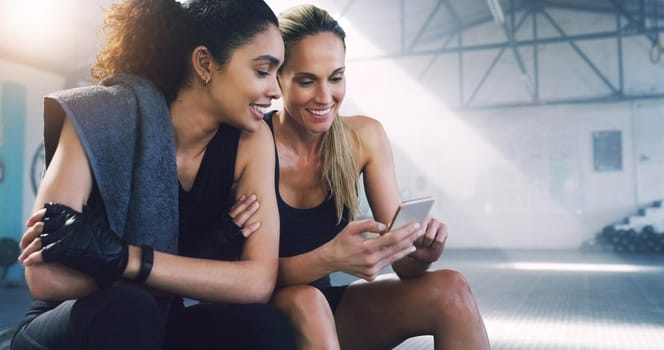 Cropped shot of two attractive sportswomen in the gym sitting down and reading text messages.