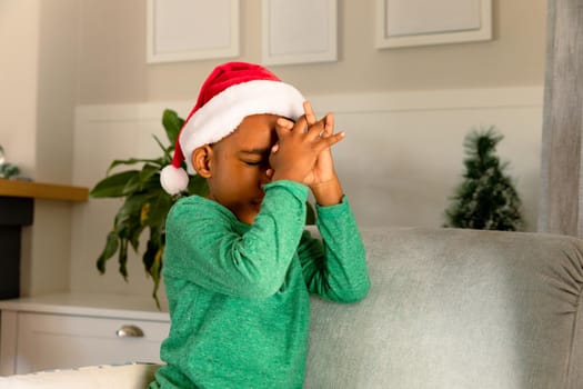 African american boy wearing santa hat and praying at christmas time. childhood, christmas, festivity and tradition at home.