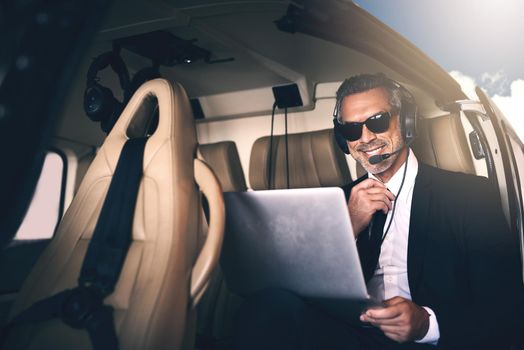 Shot of a mature businessman using a laptop while traveling in a helicopter.