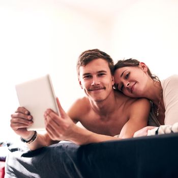 Portrait of a young couple spending a lazy day in bed with their tablet.