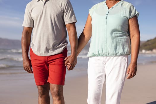 Mid section of african american couple holding hands standing on the beach. travel vacation retirement lifestyle concept