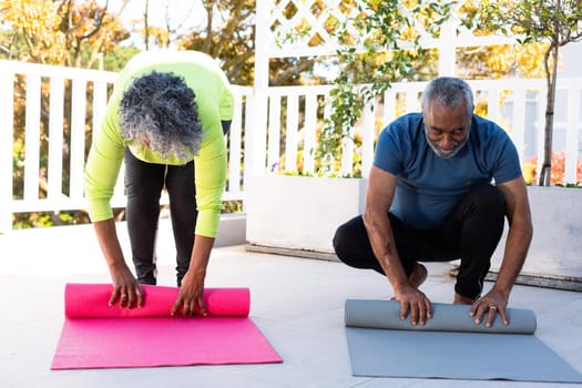 Smiling african american senior couple rolling yoga mats in garden. active and healthy retirement lifestyle at home.