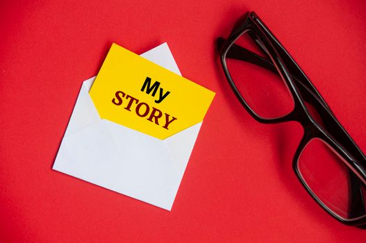 My story text on yellow notepad in an envelope. Glasses and red cover background. Conceptual