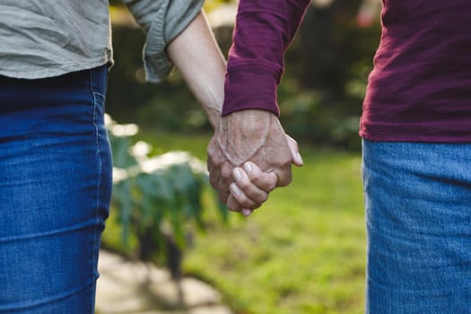 Midsection of senior caucasian couple holding hands walking in garden. retirement lifestyle, spending time at home.