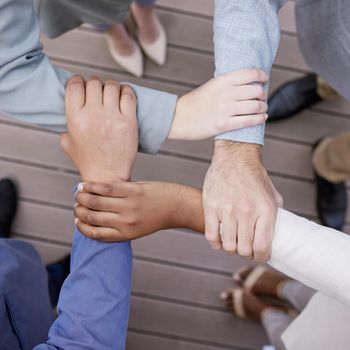 Cropped shot of a group of unrecognizable businesspeople linking arms.