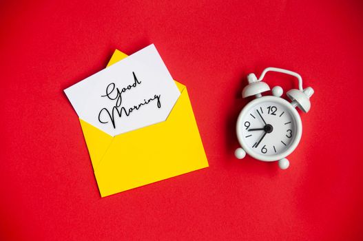 Good morning text on white notepad with envelope and alarm clock background. Morning concept