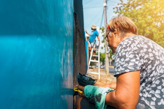 Active elderly Latin woman working outdoors painting the walls of her house with her daughter