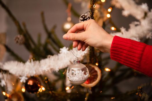 A woman's hand hangs a Christmas tree bauble to decorate the tree according to tradition in Poland. An annual Christmas ritual.