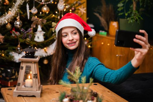 A happy and smiling teenager takes a selfie with her cell phone during the Christmas season.