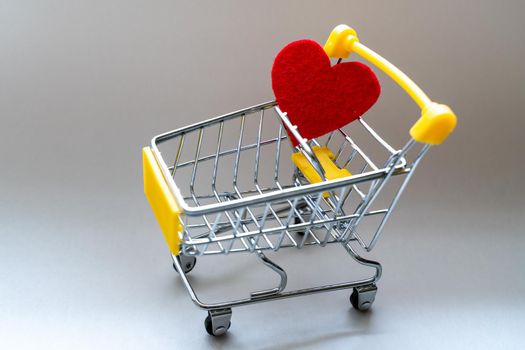 Shopping basket on a gray background with a bright red heart. Close-up
