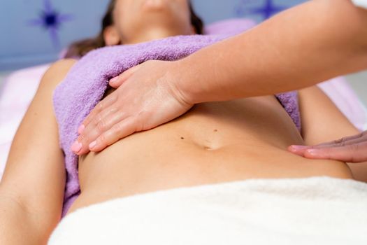 Top view of hands massaging female abdomen.Therapist applying pressure on belly. Woman receiving massage at spa salon.