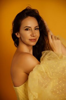 Profile portrait of a beautiful middle-aged woman in a yellow dress, her hair pulled up against a yellow background.