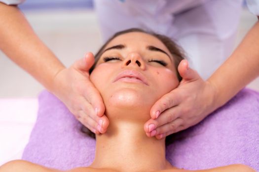 Relaxing massage. European woman getting facial massage in spa salon, side view.