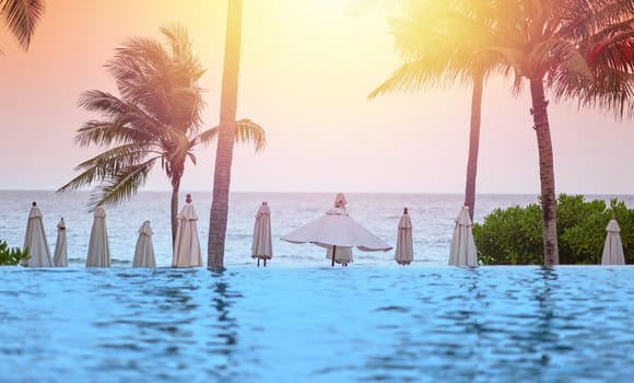 Beach front with water pool ,coconut tree,umbrella,bush,blur swimmer on sunset orange sky background and sea wave