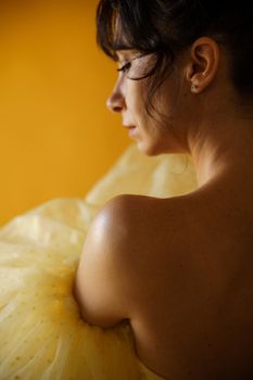 Profile portrait of a beautiful middle-aged woman in a yellow dress, her hair pulled up against a yellow background.