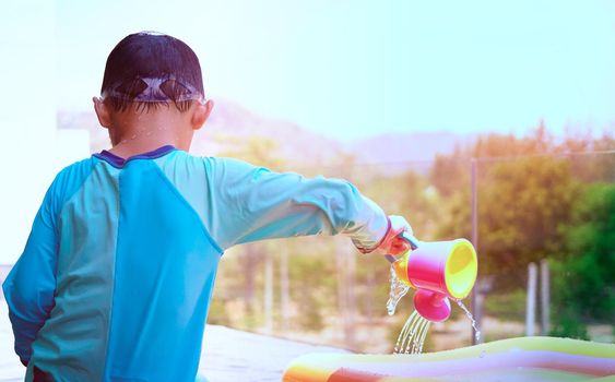 boy plays water pouring on poolside in swimming pool with sun light in summer vacation time