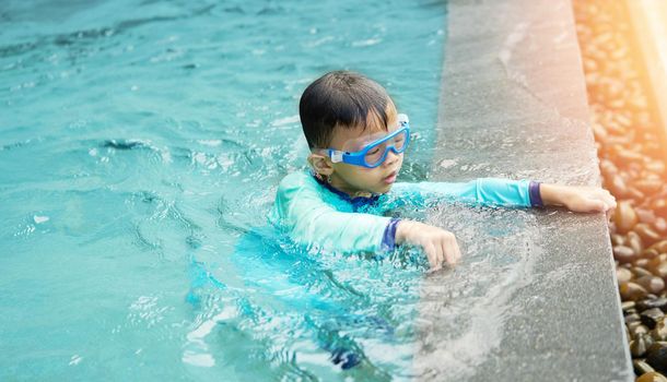 Boy plays water alone beside pool in summer concept with sun