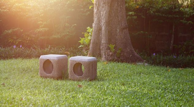 Stone chairs on green grass in park or garden on nature background with sun