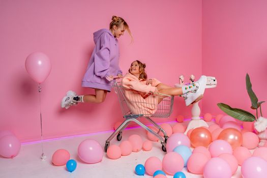 Two beautiful attractive funny joyful cheerful relaxed carefree girls dressed in casual fashion clothes isolated on hot pink background.