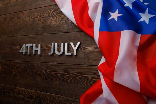 the words 4th july and crumpled usa flag on flat textured wooden surface background.